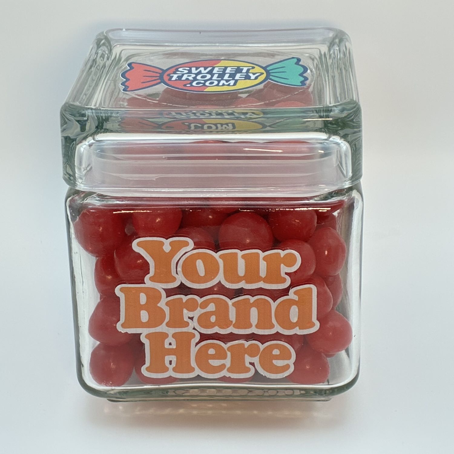Clear glass candy  jar filled with cherry sours, branded Sweet Trolley on a white background.